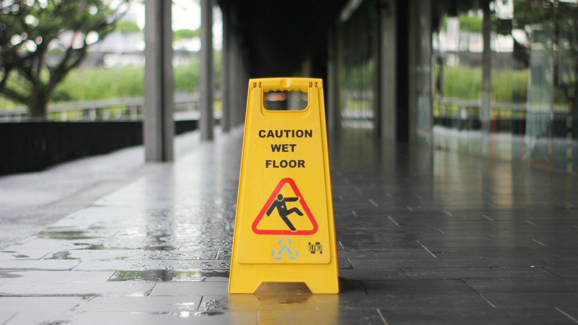 A yellow “Caution wet floor” sign standing on a wet, reflective tiled walkway.