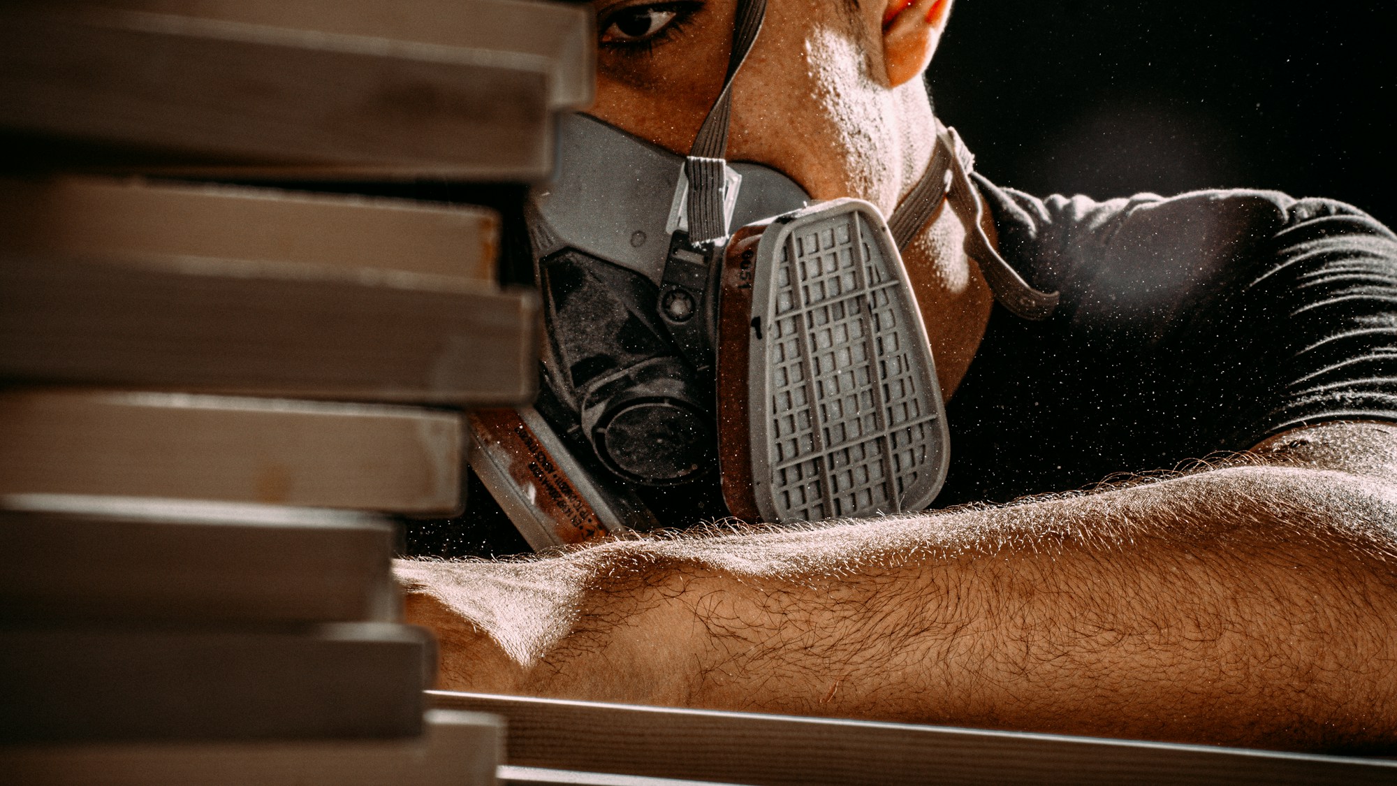A worker wearing a half-face respirator with particulate filter cartridges, with fine dust visible in the air around them.